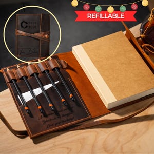 May include: A brown leather journal with a matching pen holder and a refillable notebook. The journal is embossed with a logo and the word "Refillable" is displayed on a red banner. The pen holder contains several black pens.