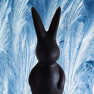 Puede incluir: Una figurita de conejo de cerámica negra con un diseño sencillo. El conejo está de pie sobre un fondo azul y blanco.