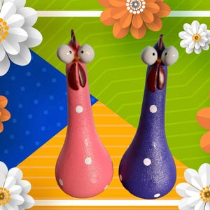 Könnte beinhalten: Zwei Keramikhühner mit großen Augen und Punkten. Ein Huhn ist rosa und das andere lila.