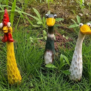 Puede incluir: Tres decoraciones de jardín caprichosas: un pollo amarillo, un pato blanco y negro y un pato blanco con pico amarillo. Los patos tienen ojos grandes de dibujos animados.