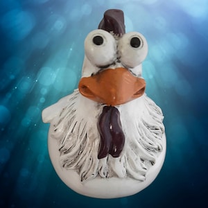 Könnte beinhalten: Eine weiße Keramik-Hühnerfigur mit großen, runden Augen, einem braunen Schnabel und einem violetten Kamm. Das Huhn hat einen weißen, flauschigen Körper und einen violetten Kehllappen.
