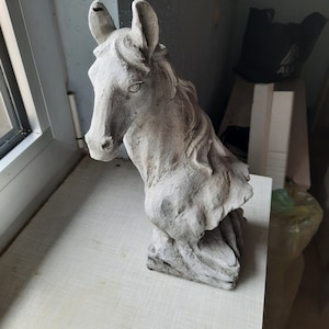 Puede incluir: Una estatua de caballo de hormigón gris con una crin detallada y una superficie texturizada.
