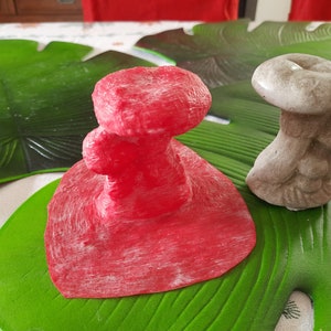 Puede incluir: Dos figuritas de hongo decorativas, una roja y otra gris, sobre un fondo de hoja verde.