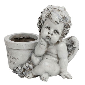 Könnte beinhalten: Ein weißer Keramik-Pflanztopf in Form eines Cherubins mit Flügeln. Der Topf hat einen kleinen Topf auf der Rückseite und die Worte "Wir vermissen Dich" sind auf der Vorderseite eingraviert.