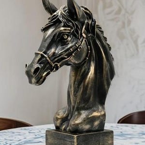 Może przedstawiać: Czarno-złota rzeźba głowy konia z uzdą. Rzeźba stoi na czarnej podstawie.