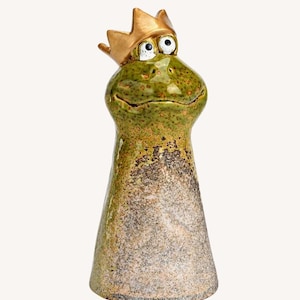 Könnte beinhalten: Eine skurrile Keramikfroschfigur mit goldener Krone. Der Frosch hat einen grün-braun gesprenkelten Körper und einen lächelnden Gesichtsausdruck. Die Figur ist etwa 15 cm hoch und hat eine strukturierte, gesprenkelte Oberfläche.