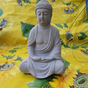 May include: A gray stone statue of a meditating Buddha sitting in a lotus position. The statue has a serene expression and is decorated with small dots on the head.