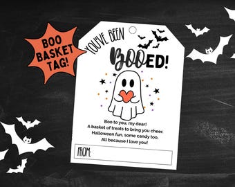 Puede incluir: Una etiqueta de regalo blanca con temática de Halloween con el texto "YOU'VE BEEN BOOED!" y un fantasma de dibujos animados sosteniendo un corazón. Una etiqueta naranja en forma de estrella dice "BOO BASKET TAG!".