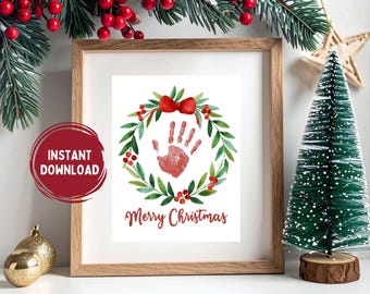 Puede incluir: Impresión enmarcada con un diseño de corona navideña en acuarela. La corona presenta hojas verdes, bayas rojas y una huella de mano roja. Las palabras "Merry Christmas" están escritas debajo en rojo. Un círculo rojo con "Descarga instantánea".