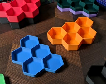 May include: A set of six hexagonal shaped trays in various colors, including blue, orange, red, and black. The trays are made of plastic and have a honeycomb design.
