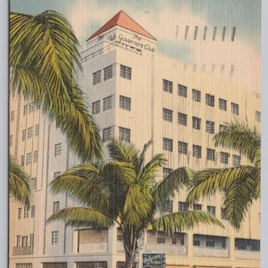 May include: Vintage postcard featuring The Governors' Club Hotel in Fort Lauderdale, Florida. The image shows a multi-story building with a red-roofed tower, palm trees, and classic cars. The text "The Governors' Club" is visible on the building.