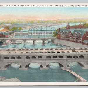 May include: Vintage postcard featuring a scenic view of Broad Street and Court Street Bridges and the NY State Barge Canal Terminal in Rochester, NY. The image showcases multiple bridges over a river, with buildings and a distant landscape under a blue sky.