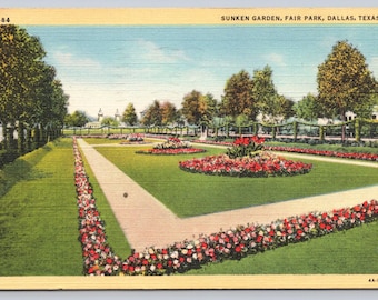 May include: Vintage postcard of the Sunken Garden in Fair Park, Dallas, Texas. The image shows a formal garden with a central path, flower beds, and trees. The sky is blue with some clouds. The postcard has a yellowed border.