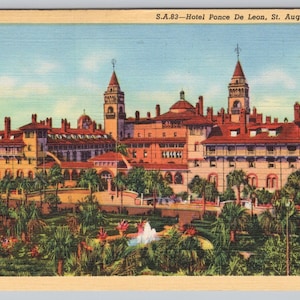 May include: Vintage postcard featuring the Hotel Ponce De Leon in St. Augustine, Florida. The image shows a large, ornate building with multiple towers and red tile roofs, surrounded by lush greenery and palm trees. The sky is a light blue.