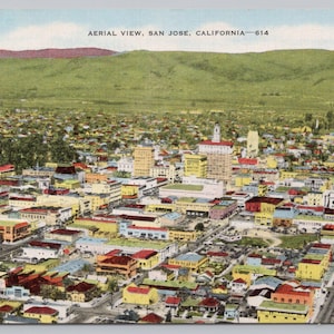 May include: Vintage postcard with an aerial view of San Jose, California. The image shows a densely populated city with various buildings and structures, set against a backdrop of green hills and a blue sky. The text "AERIAL VIEW, SAN JOSE, CALIFORNIA - 614" is visible.