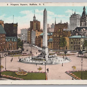 May include: Vintage postcard featuring Niagara Square in Buffalo, N.Y. The image showcases a large obelisk monument in the center of a circular plaza, surrounded by buildings and a streetcar. The postcard has a faded color palette, typical of its era.