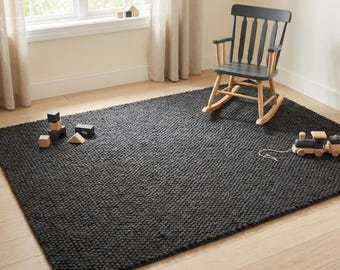 Puede incluir: Una alfombra de color gris carbón oscuro con una superficie texturizada de nudos. Una mecedora de madera gris oscuro con detalles en madera clara se encuentra sobre la alfombra. Varios bloques de construcción y un tren de juguete están sobre ella.