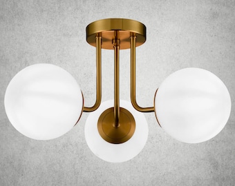 May include: A gold ceiling light fixture with three white globe-shaped shades. The fixture has a modern design with curved arms.