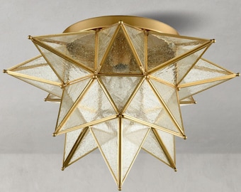 May include: A star-shaped flush mount ceiling light fixture featuring a metallic gold frame and textured, seeded glass panels. The geometric design consists of multiple triangular glass segments arranged in a multi-pointed star formation.