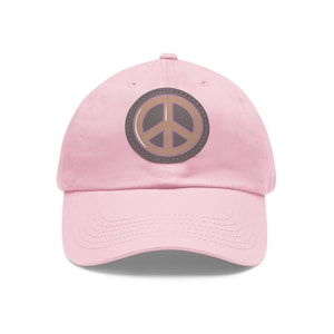 Puede incluir: Una gorra de béisbol rosa con un parche de signo de paz marrón.