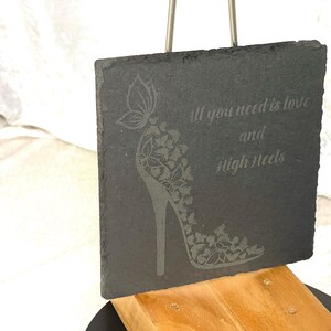 Könnte beinhalten: Schwarzes Schiefer-Schild mit einem weißen High-Heel-Schuh-Design und dem Text "Alles, was du brauchst, ist Liebe und High Heels".