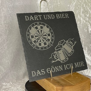 May include: A black slate sign with the text "DART UND BIER" and a dartboard with two darts. Below the dartboard are two beer mugs clinking together. The text "DAS GÖNN ICH MIR" is at the bottom of the sign.