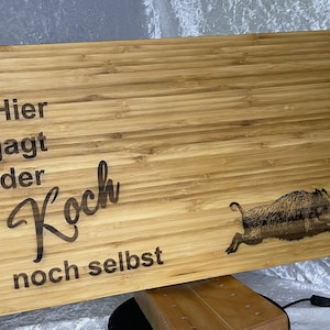 May include: A brown wooden chopping board with the text "Hier jagt der Koch noch selbst" and a black and white image of a wild boar running to the right.