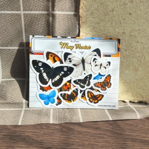 Peut inclure: Une feuille d'autocollants représentant des papillons colorés. Les autocollants sont disposés en grille et présentent différentes espèces de papillons. La feuille est intitulée "Go Wild & Free May Florist".