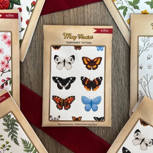 May include: A pack of temporary tattoos featuring colorful butterfly designs. The pack is labeled "May Florist Temporary Tattoos" and includes the social media handle "@gowildandfree".
