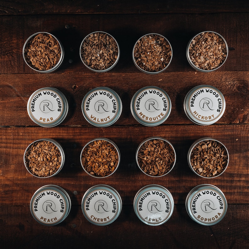 May include: Twelve round metal containers with lids, each containing wood chips for smoking. The containers are labeled with the type of wood, including Pear, Walnut, Mesquite, Hickory, Peach, Cherry, Apple, and Sophora.