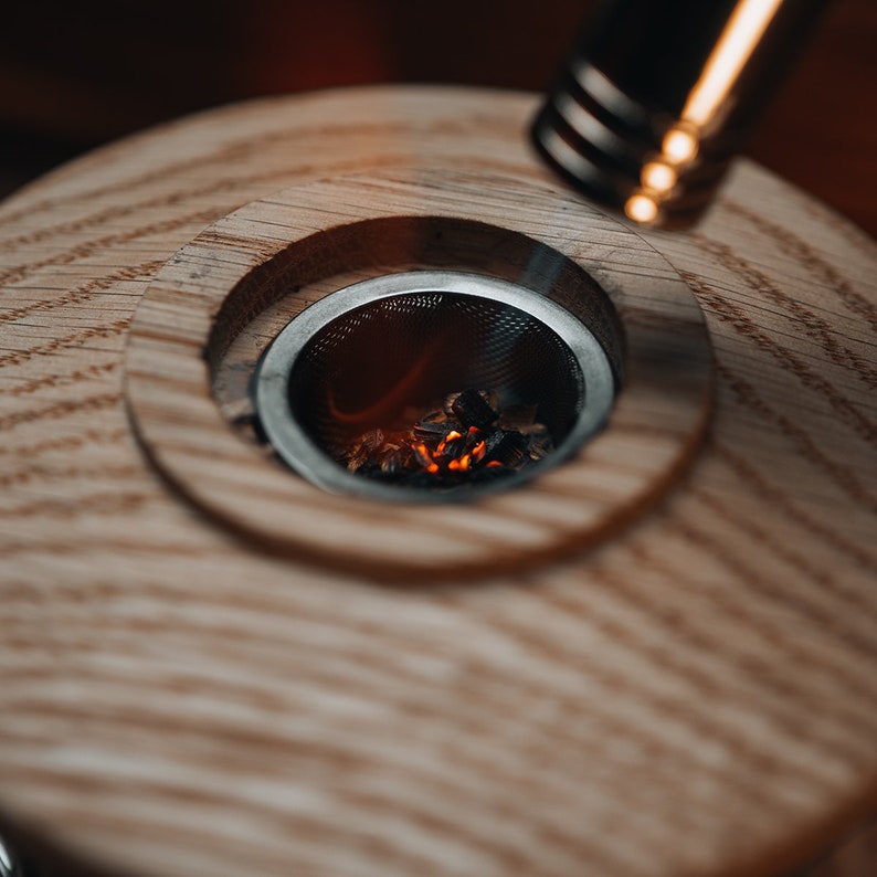 May include: A close-up of a wooden smoking pipe with a metal mesh bowl. The bowl is filled with glowing charcoal.