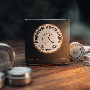 May include: A black box with the text "PREMIUM WOOD CHIPS" in a circle with a stylized "R" in the center. The box is labeled "CRAFTED GOODS" and "BY RONYX". There are several small silver containers with the same logo in the background.