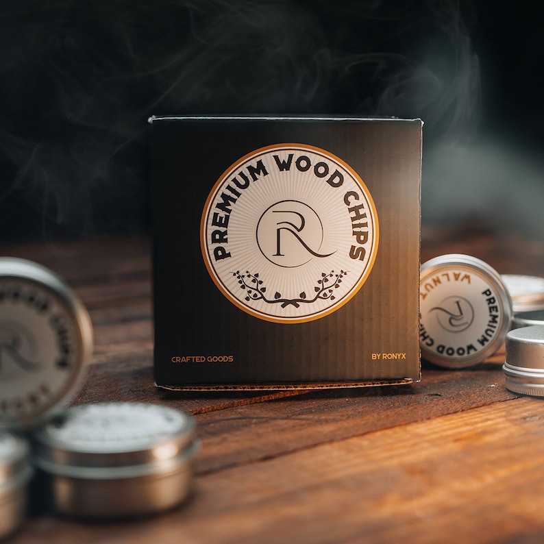 May include: A black box with the text "PREMIUM WOOD CHIPS" in a circle with a stylized "R" in the center. The box is labeled "CRAFTED GOODS" and "BY RONYX". There are several small silver containers with the same logo in the background.