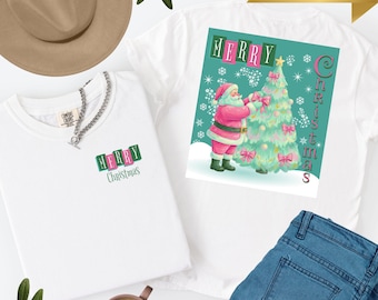 Puede incluir: Dos camisetas blancas con diseños navideños. Una muestra a Papá Noel decorando un árbol, la otra tiene la inscripción "MERRY Christmas". Un sombrero marrón, una cadena plateada y una taza de café también están presentes.