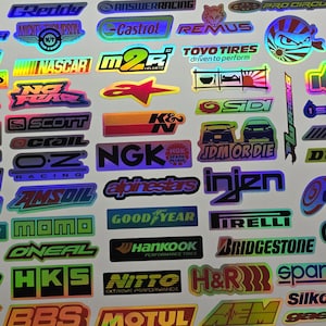 May include: A collection of holographic stickers featuring various brand logos and graphics. The stickers include logos for racing, automotive, and performance brands, with vibrant colors and reflective surfaces.