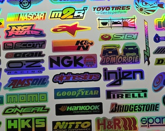 May include: A collection of holographic stickers featuring various brand logos and graphics. The stickers include logos for racing, automotive, and performance brands, with vibrant colors and reflective surfaces.