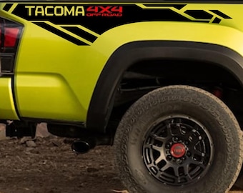May include: A section of a lime green truck bed with black and yellow geometric decals. The decals include the text "TACOMA 4X4 OFF ROAD" in black and red. A black tire and wheel are visible.