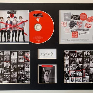 Puede incluir: Enmarcado conmemorativo musical con un CD y fotos de la banda 5 Seconds of Summer. El CD es rojo y las imágenes incluyen fotos de la banda y arte del álbum. El marco es negro.
