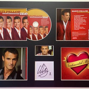 Puede incluir: Exhibición enmarcada del álbum "Sentimental Me" de Marti Pellow. Incluye un CD, carátulas de álbum, una foto firmada y otras imágenes de Pellow. La carátula del álbum presenta un corazón rojo con una cinta dorada.
