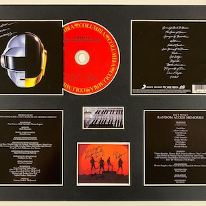 May include: Framed Daft Punk "Random Access Memories" album art, CD, and signed photo. The album cover features a silver and gold helmet. The CD is red with "Columbia" branding. The signed photo shows the band's silhouette.