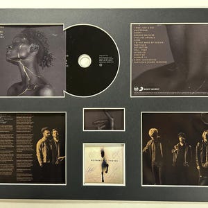 May include: Framed CD and album art from Nothing But Thieves' album, 'Broken Machine'. The display includes the CD, album cover art, lyrics, and band photos. The album cover features a woman with gold accents.