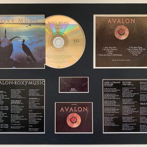 May include: A framed display of the Roxy Music album Avalon. The display includes the album cover, a CD, and lyric sheets. The album cover features a black raven perched on a helmet with a crown. The CD is gold with the album title printed on it. The lyric sheets are printed on white paper and include the lyrics for each song on the album. The album title "Avalon" is printed in white on a black background.