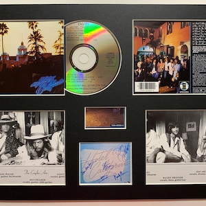 May include: Framed Eagles "Hotel California" album display. Includes a CD, album art, and band member photos. The display features the album title and band signatures. The frame is black.