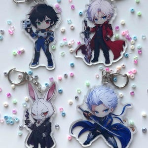 Peut inclure: Quatre porte-clés en acrylique représentant des personnages d'anime de style chibi. L'un tient une arme de poing, un autre une grande épée, un troisième est un lapin en costume tenant une tasse, et le dernier tient un katana. Chaque pièce inclut un fermoir mousqueton et un anneau en métal argenté.