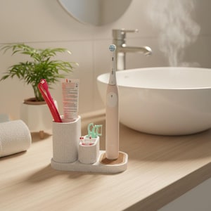 May include: A light pink electric toothbrush and a white toothbrush holder with a toothbrush, toothpaste, and floss picks. The holder sits on a wooden surface in a bathroom setting, with a white sink and a small plant.
