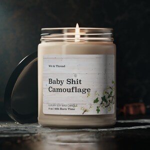 May include: A 9 ounce soy wax candle in a clear glass jar with a white label that reads "Wit & Thread Baby Shit Camouflage Luxury Soy Wax Candle 9 oz | 60h Burn Time".