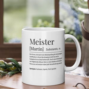 Puede incluir: Taza de cerámica blanca con una definición negra de la palabra "Meister" con el nombre "Martin" entre paréntesis. La definición está en alemán e incluye la palabra "Substantiv", que significa sustantivo.