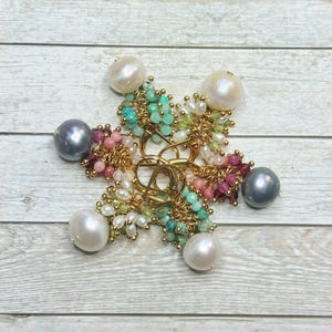 May include: A star-shaped jewellery piece with a gold-tone centre and six pearl accents. The piece is adorned with clusters of colourful beads in shades of pink, green, and turquoise. The pearls are large and white, and the beads are small and round.