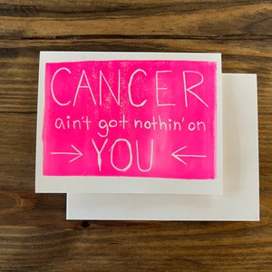 May include: A pink card with white text that reads "Cancer ain't got nothin' on YOU" with arrows pointing to the word "YOU".