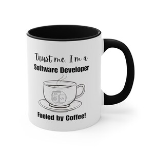 May include: White ceramic coffee mug with a black rim and handle. The mug has a black design that says "Trust me. I'm a Software Developer Fueled by Coffee!" and a cartoon image of a coffee cup with code inside.